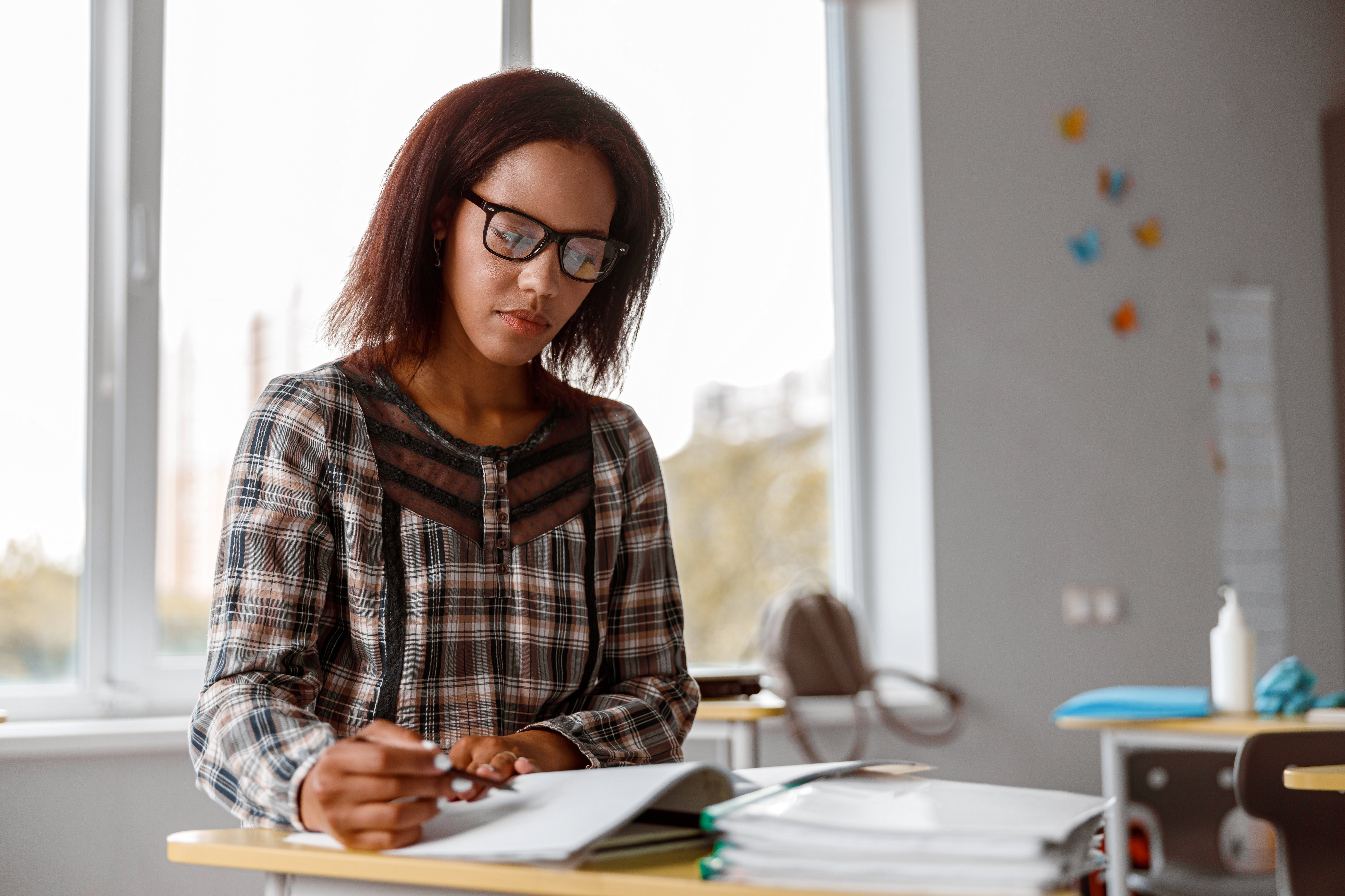 Afro American teacher in glasses sitting at a desk and writing