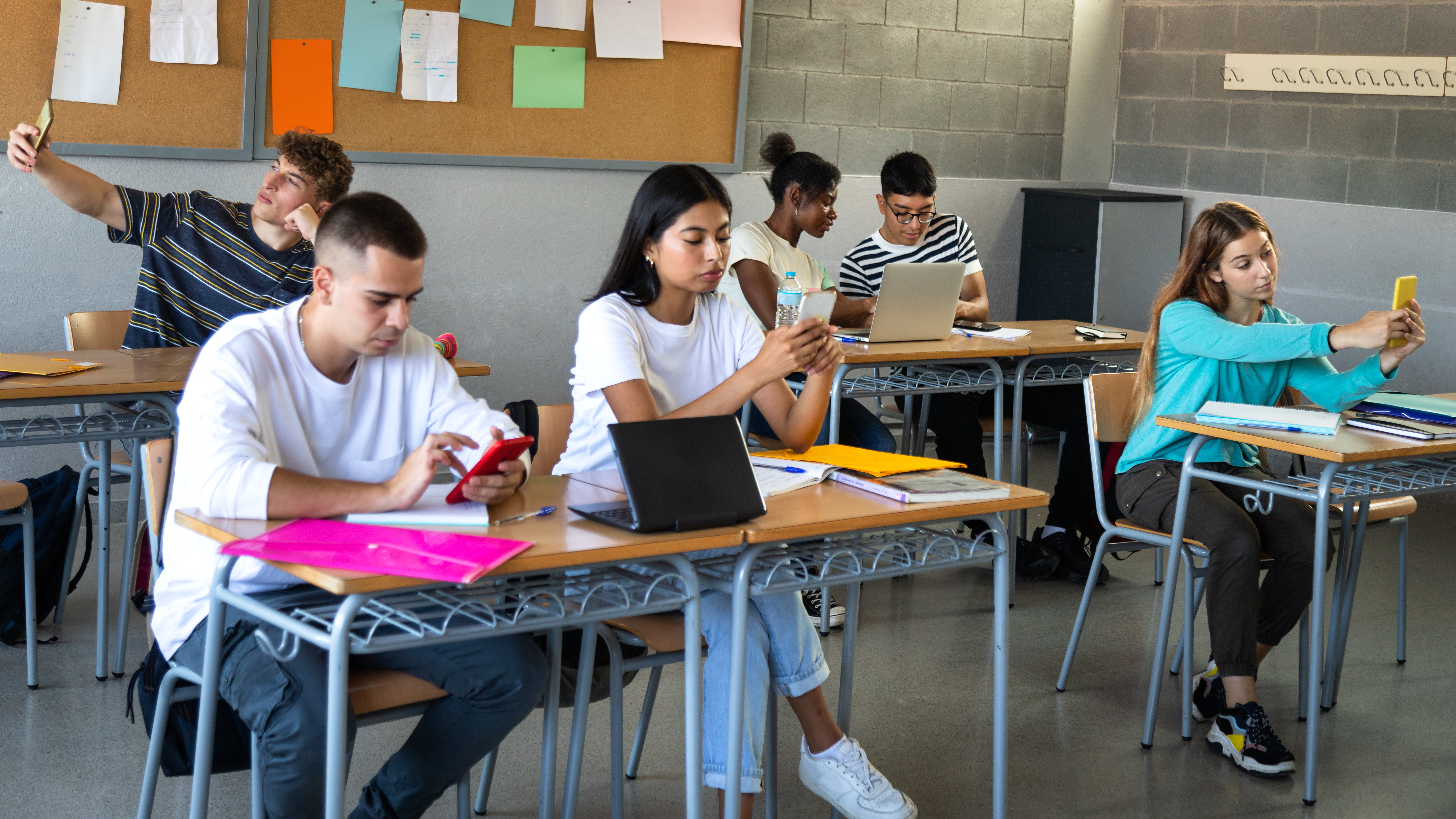 Multiracial high school students distracted from lesson using mobile phones in class.