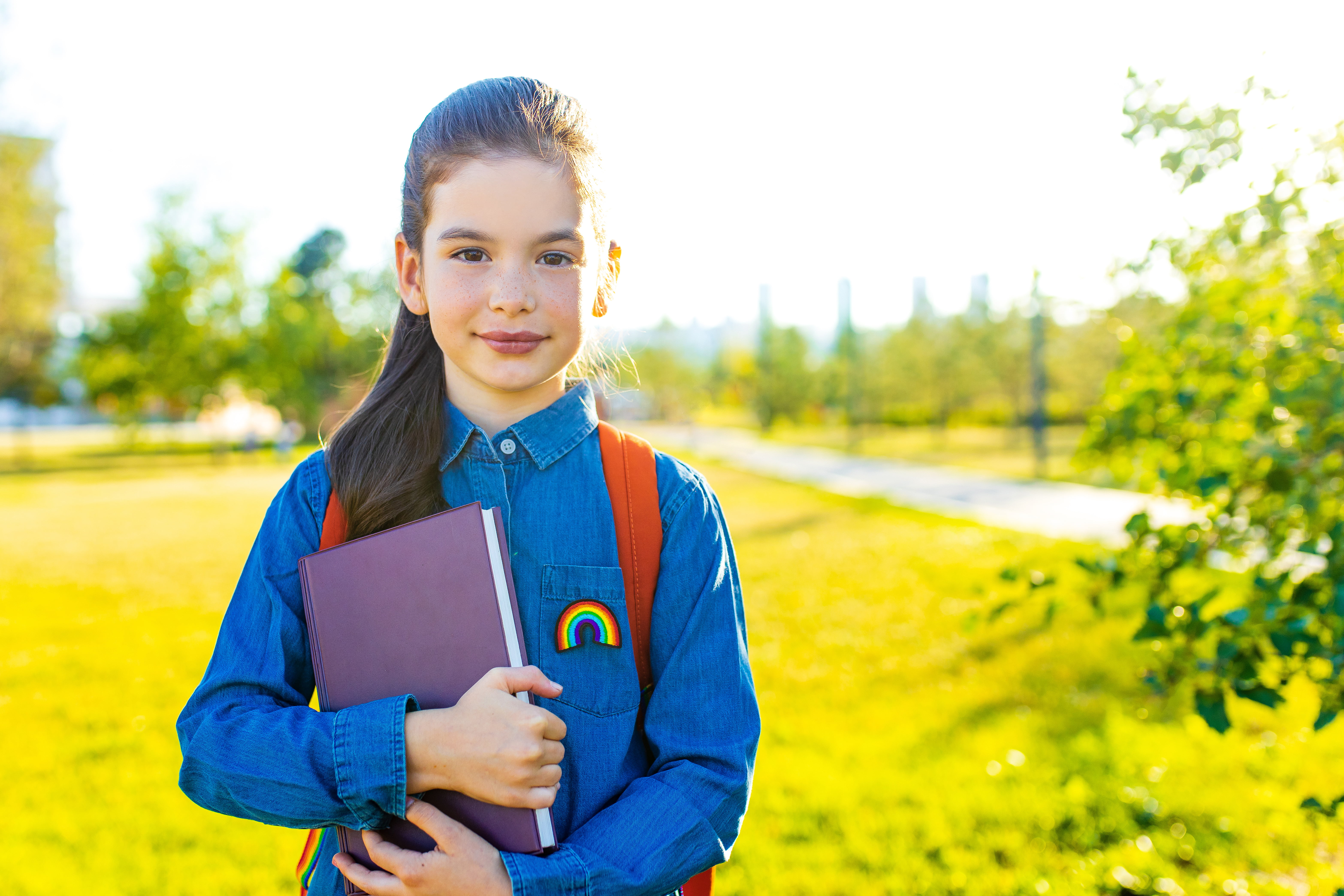 Smiling indian student girl wearing school backpack and blue t-shirt in park