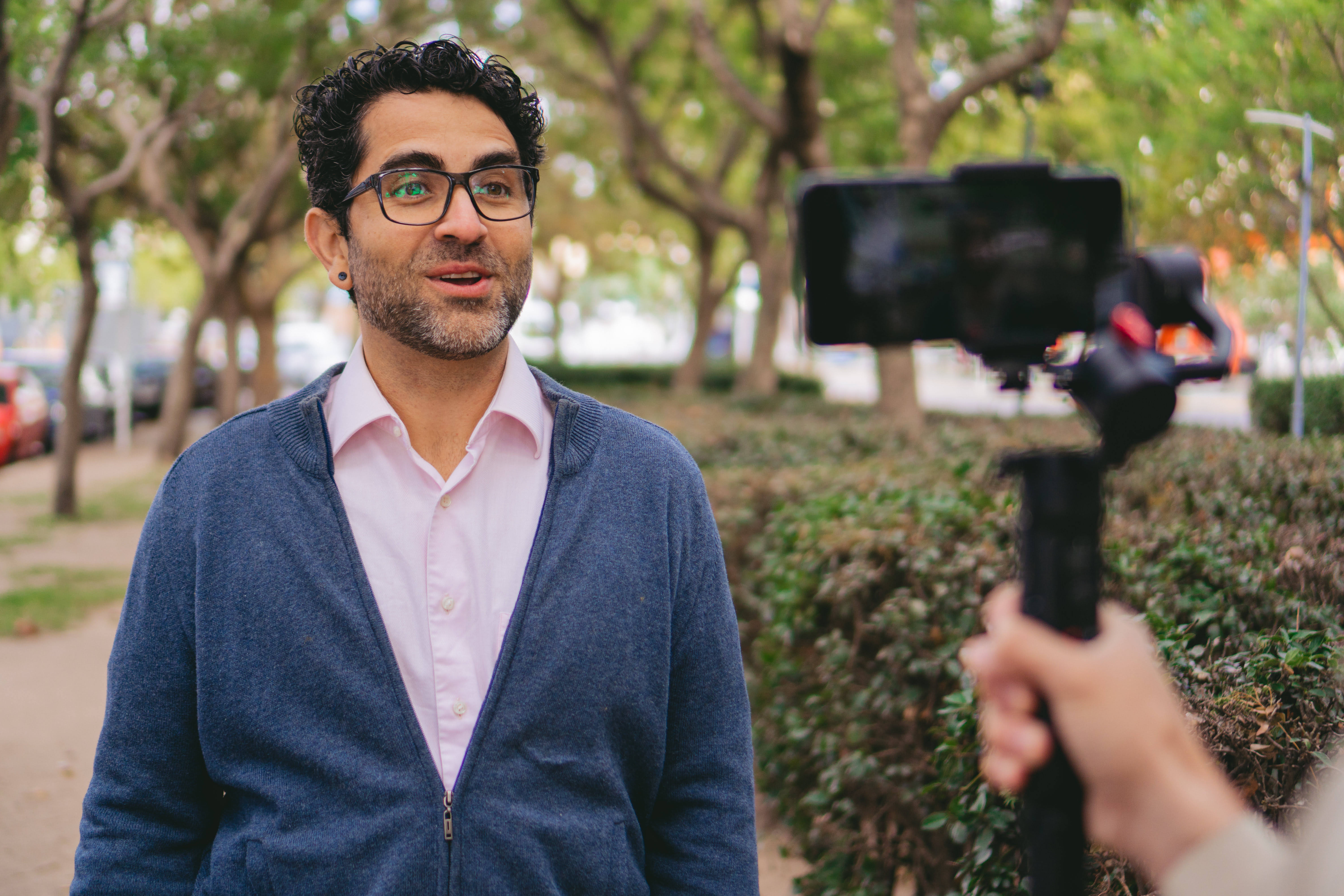 middle-aged Latin man shooting a video for social media with a camera assistant in a city park.