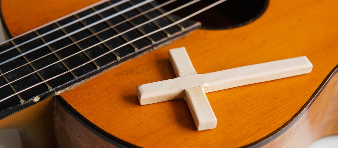 Acoustic guitar with wooden cross on the table close up. Christian music.